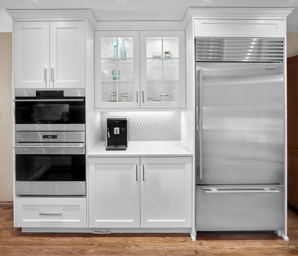 Mid-sized transitional l-shaped medium tone wood floor and brown floor eat-in kitchen photo in Edmonton with a farmhouse sink, recessed-panel cabinets, white cabinets, quartz countertops, gray backsplash, glass tile backsplash, stainless steel appliances and no island