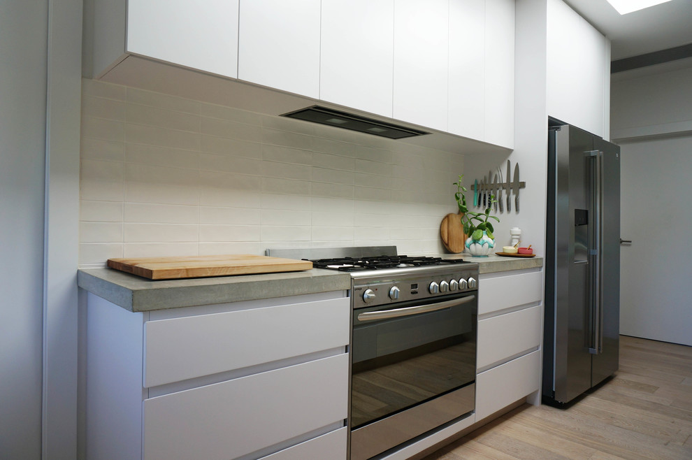 Photo of a modern open plan kitchen in Melbourne with flat-panel cabinets, white cabinets, concrete benchtops, white splashback, with island, stainless steel appliances and light hardwood floors.