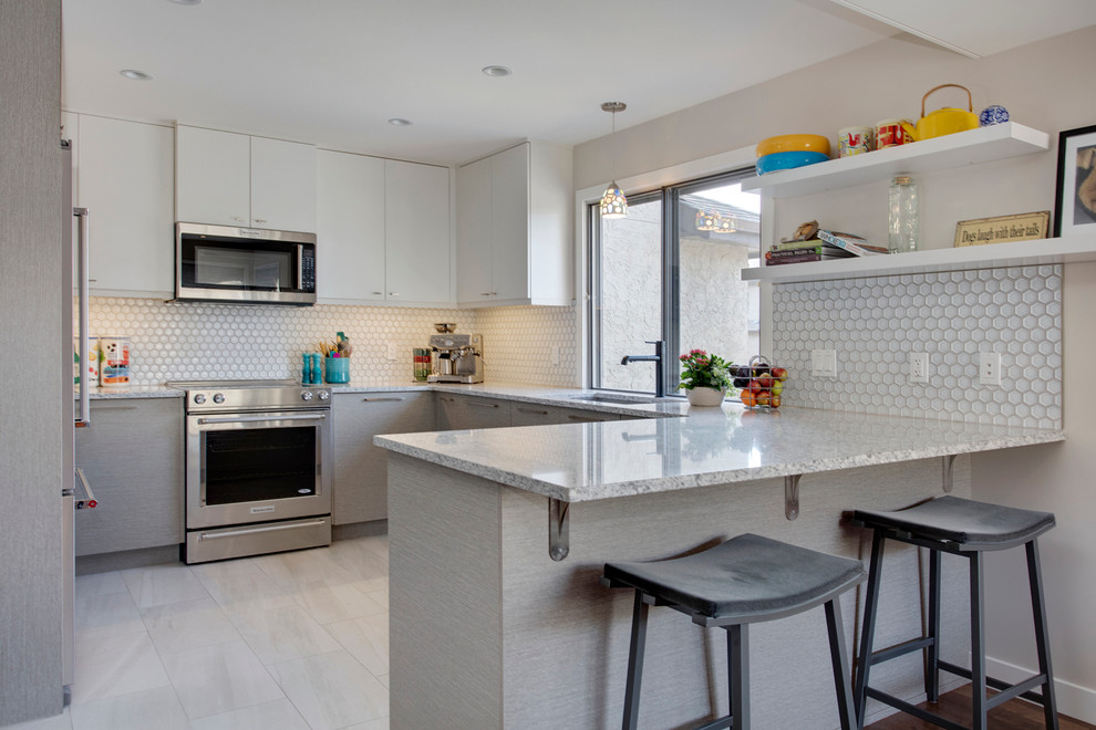 Photo of a contemporary u-shaped eat-in kitchen in Calgary with an undermount sink, flat-panel cabinets, grey cabinets, granite benchtops, grey splashback, mosaic tile splashback, stainless steel appliances, porcelain floors and a peninsula.