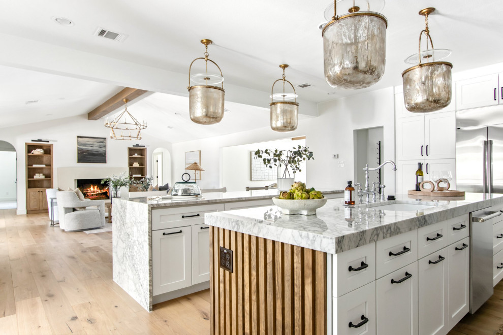 Huge transitional light wood floor and brown floor open concept kitchen photo in Dallas with shaker cabinets, white cabinets, white backsplash, stainless steel appliances, two islands, white countertops, a farmhouse sink, marble countertops and marble backsplash