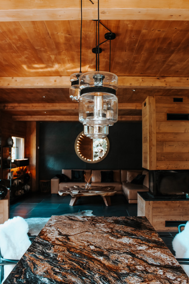Inspiration for an expansive rustic open plan living room in Other with black walls, slate flooring, a two-sided fireplace, a wooden fireplace surround, a freestanding tv, black floors, a wood ceiling, wood walls and feature lighting.