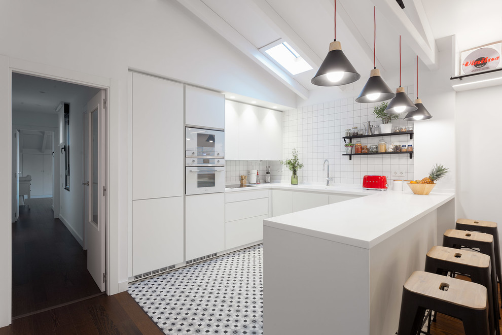 Photo of a contemporary u-shaped kitchen in Other with flat-panel cabinets, white cabinets, white splashback, white appliances, a peninsula, white benchtop and grey floor.