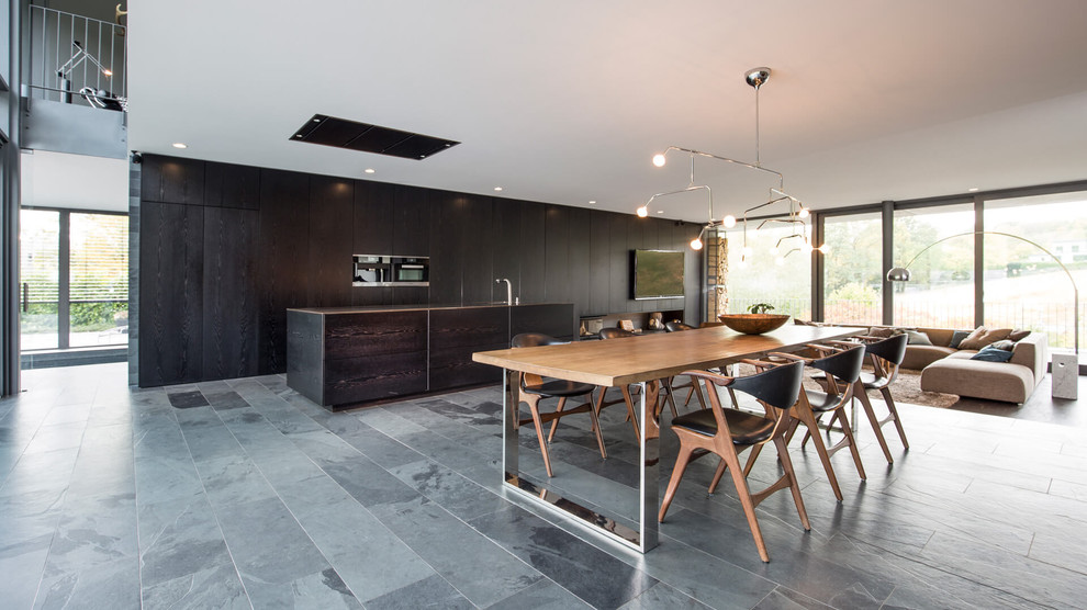 This is an example of an expansive contemporary dining room in Dortmund with white walls, slate floors, a two-sided fireplace, a wood fireplace surround and grey floor.