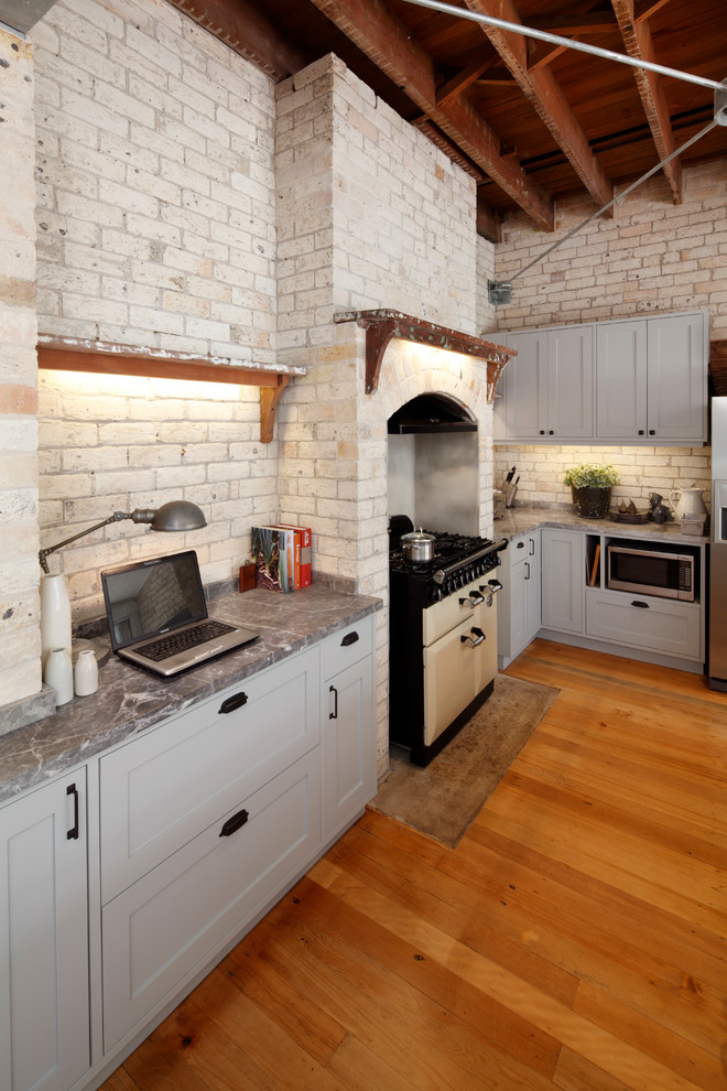 Photo of an industrial l-shaped eat-in kitchen in Sydney with an undermount sink, grey cabinets, marble benchtops, beige splashback, stainless steel appliances, medium hardwood floors and with island.