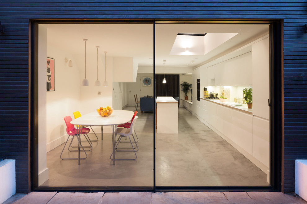 Design ideas for a mid-sized contemporary single-wall open plan kitchen in London with flat-panel cabinets, white cabinets, white splashback, concrete floors, with island, grey floor and white benchtop.