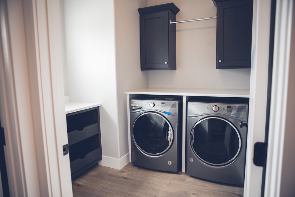 Design ideas for a mid-sized contemporary l-shaped dedicated laundry room in Other with shaker cabinets, black cabinets, grey walls, medium hardwood floors, a side-by-side washer and dryer and brown floor.