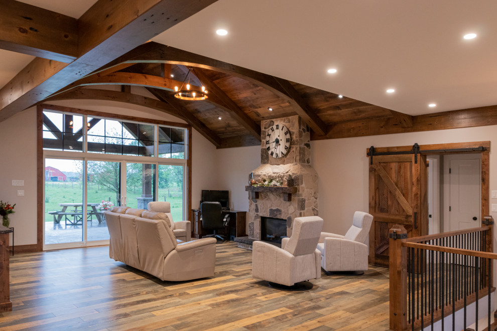 Photo of a mid-sized country open concept family room in Toronto with beige walls, medium hardwood floors, a standard fireplace, a stone fireplace surround, no tv, multi-coloured floor and vaulted.