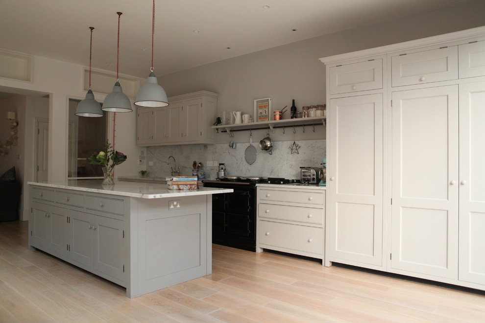 Design ideas for a mid-sized traditional single-wall open plan kitchen in London with shaker cabinets, marble benchtops, with island, an integrated sink, grey cabinets, grey splashback, stone slab splashback, black appliances and light hardwood floors.