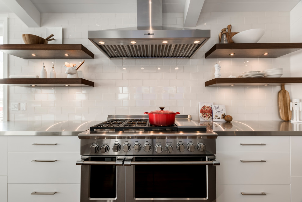 Inspiration for a mid-sized transitional single-wall medium tone wood floor open concept kitchen remodel with an undermount sink, flat-panel cabinets, white cabinets, stainless steel countertops, white backsplash, stainless steel appliances, an island and ceramic backsplash
