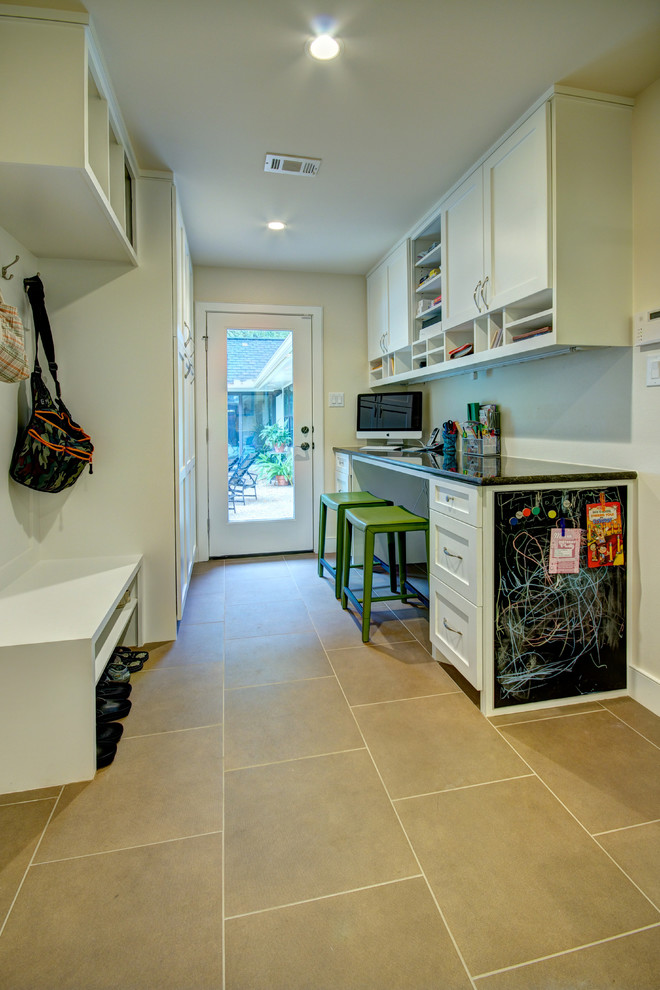 Inspiration for a mid-sized transitional galley utility room in Austin with shaker cabinets, white cabinets, granite benchtops, beige walls, limestone floors and a stacked washer and dryer.