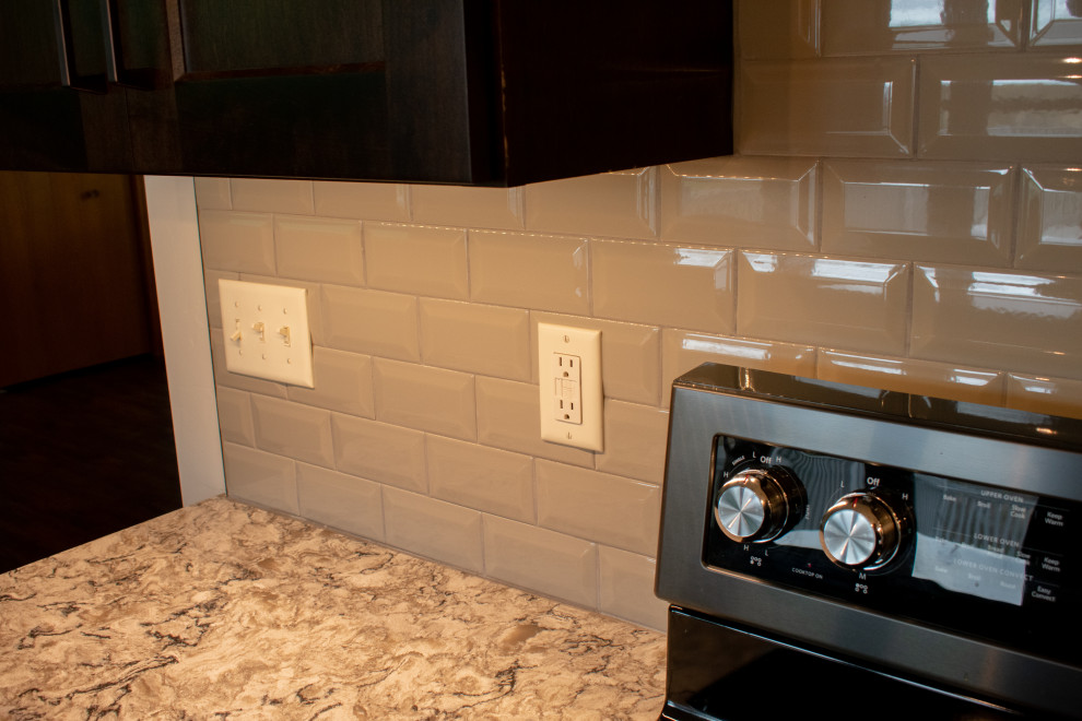 Example of a large transitional l-shaped vinyl floor, brown floor and vaulted ceiling eat-in kitchen design with an undermount sink, flat-panel cabinets, medium tone wood cabinets, quartz countertops, gray backsplash, ceramic backsplash, black appliances, an island and beige countertops