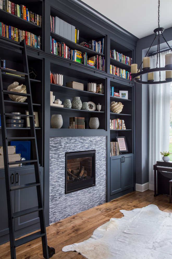 Photo of a mid-sized transitional home office in Portland with a library, black walls, medium hardwood floors, a standard fireplace, a tile fireplace surround and brown floor.