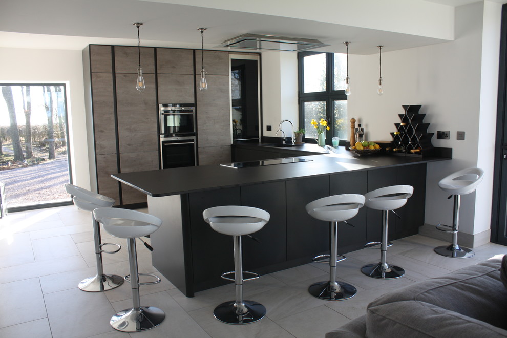 Photo of a mid-sized modern u-shaped open plan kitchen in Other with a peninsula, an undermount sink, flat-panel cabinets, grey cabinets, solid surface benchtops, grey splashback, black appliances, ceramic floors, engineered quartz splashback, grey floor, black benchtop and coffered.