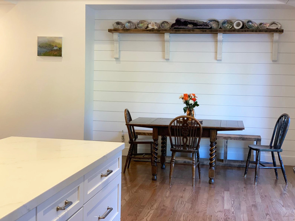 Design ideas for a mid-sized country eat-in kitchen in Other with a farmhouse sink, raised-panel cabinets, white cabinets, quartz benchtops, white splashback, stainless steel appliances, with island, brown floor and white benchtop.