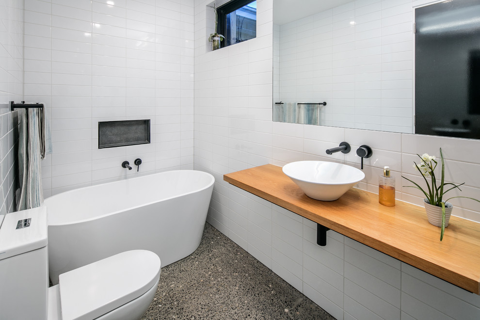 This is an example of a mid-sized bathroom in Melbourne with a console sink, glass-front cabinets, wood benchtops, a two-piece toilet, white tile, ceramic tile, white walls and concrete floors.