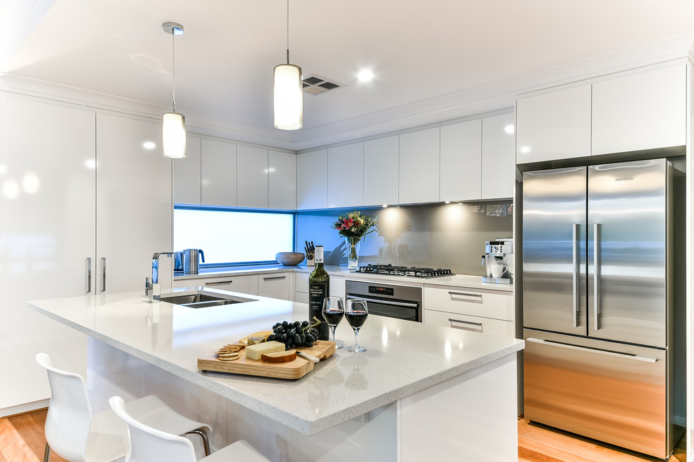 Inspiration for a mid-sized modern l-shaped eat-in kitchen in Perth with an undermount sink, flat-panel cabinets, white cabinets, quartz benchtops, metallic splashback, glass sheet splashback, stainless steel appliances, medium hardwood floors and with island.