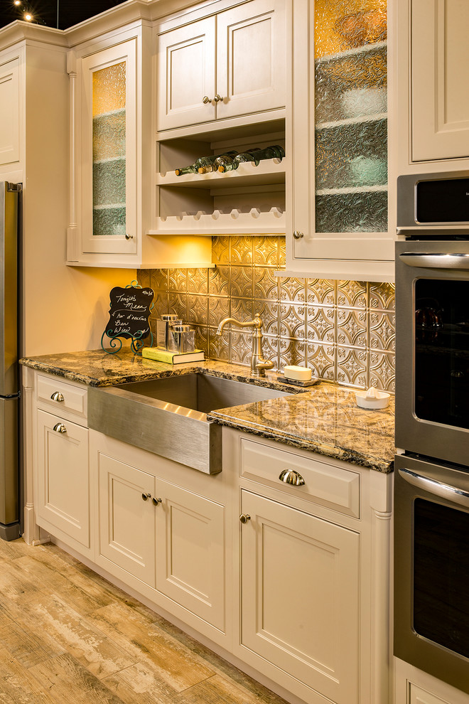 Mid-sized elegant medium tone wood floor and brown floor kitchen photo with a farmhouse sink, beaded inset cabinets, white cabinets, granite countertops, metallic backsplash, metal backsplash and stainless steel appliances