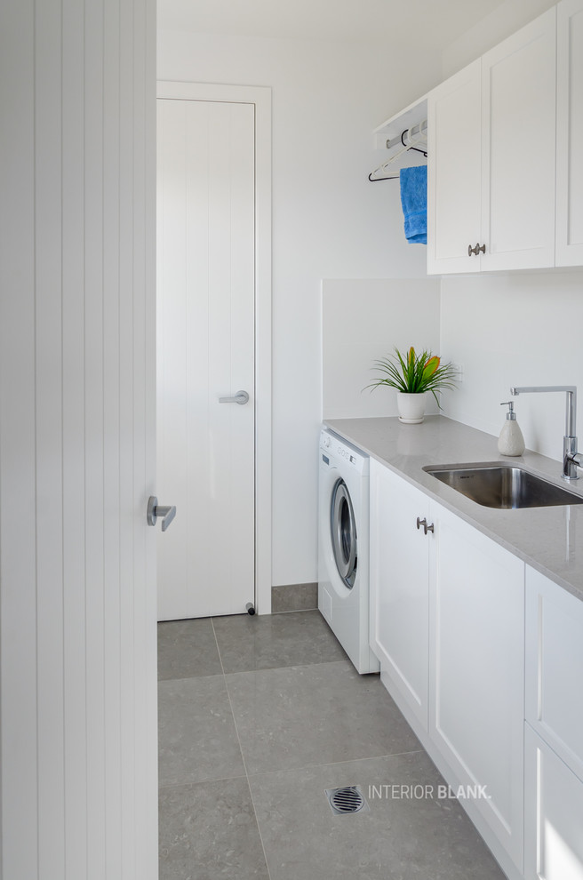 Inspiration for a beach style single-wall dedicated laundry room in Gold Coast - Tweed with an undermount sink, recessed-panel cabinets, white cabinets, quartz benchtops, white walls, porcelain floors and grey floor.