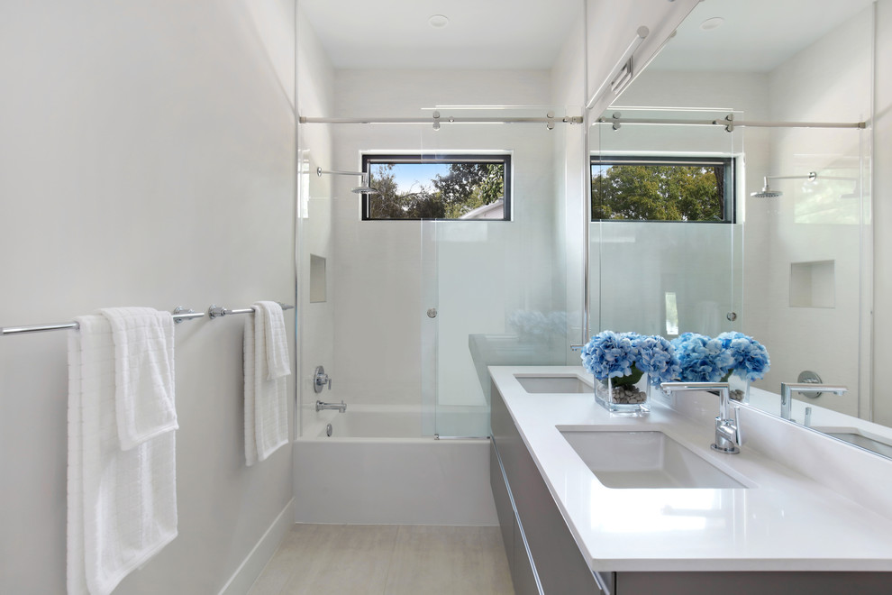 This is an example of a mid-sized contemporary kids bathroom in Tampa with flat-panel cabinets, grey cabinets, an alcove tub, white tile, porcelain tile, white walls, porcelain floors, an undermount sink, engineered quartz benchtops, a sliding shower screen, white benchtops, an alcove shower and beige floor.