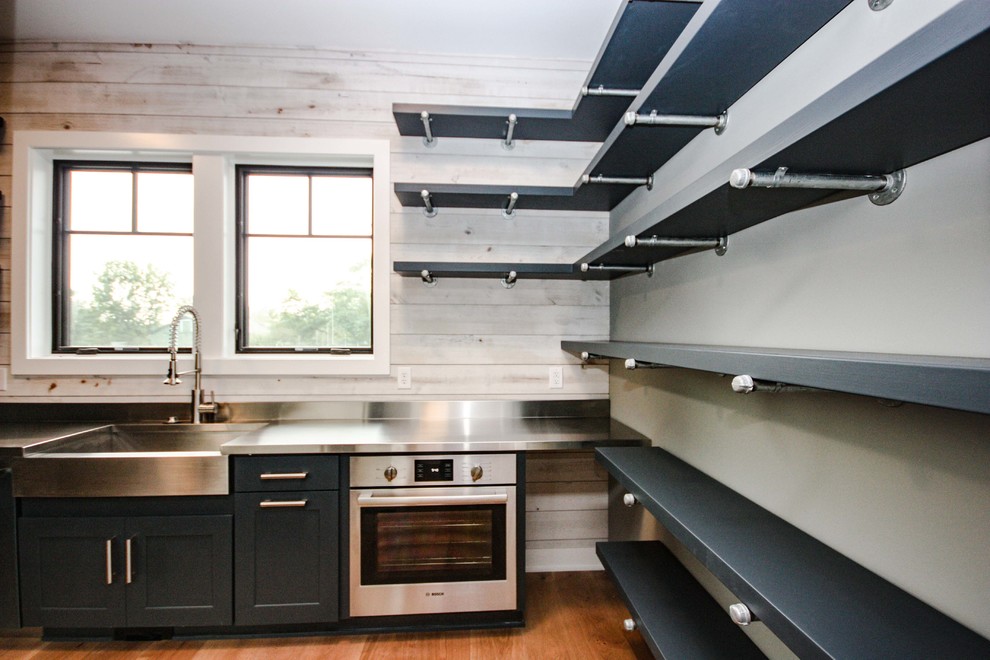 This is an example of a mid-sized industrial l-shaped separate kitchen in Indianapolis with a farmhouse sink, shaker cabinets, black cabinets, zinc benchtops, beige splashback, timber splashback, stainless steel appliances, medium hardwood floors, no island and brown floor.