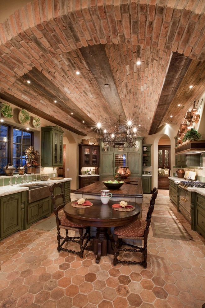 Large mediterranean u-shaped eat-in kitchen in Las Vegas with a farmhouse sink, raised-panel cabinets, green cabinets, with island, wood benchtops, green splashback, stone tile splashback, stainless steel appliances and terra-cotta floors.
