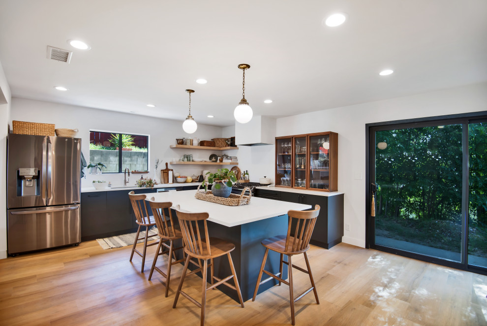 This is an example of a contemporary l-shaped kitchen in Los Angeles with an undermount sink, flat-panel cabinets, grey cabinets, stainless steel appliances, medium hardwood floors, with island, brown floor and white benchtop.