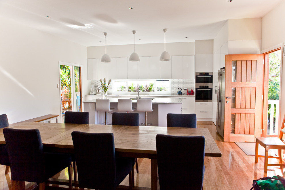 Photo of a contemporary l-shaped eat-in kitchen in Brisbane with flat-panel cabinets, white cabinets, white splashback, subway tile splashback, stainless steel appliances and marble benchtops.