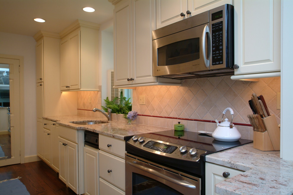 Photo of a mid-sized traditional single-wall eat-in kitchen in Philadelphia with an undermount sink, raised-panel cabinets, yellow cabinets, beige splashback, stone tile splashback, stainless steel appliances and dark hardwood floors.