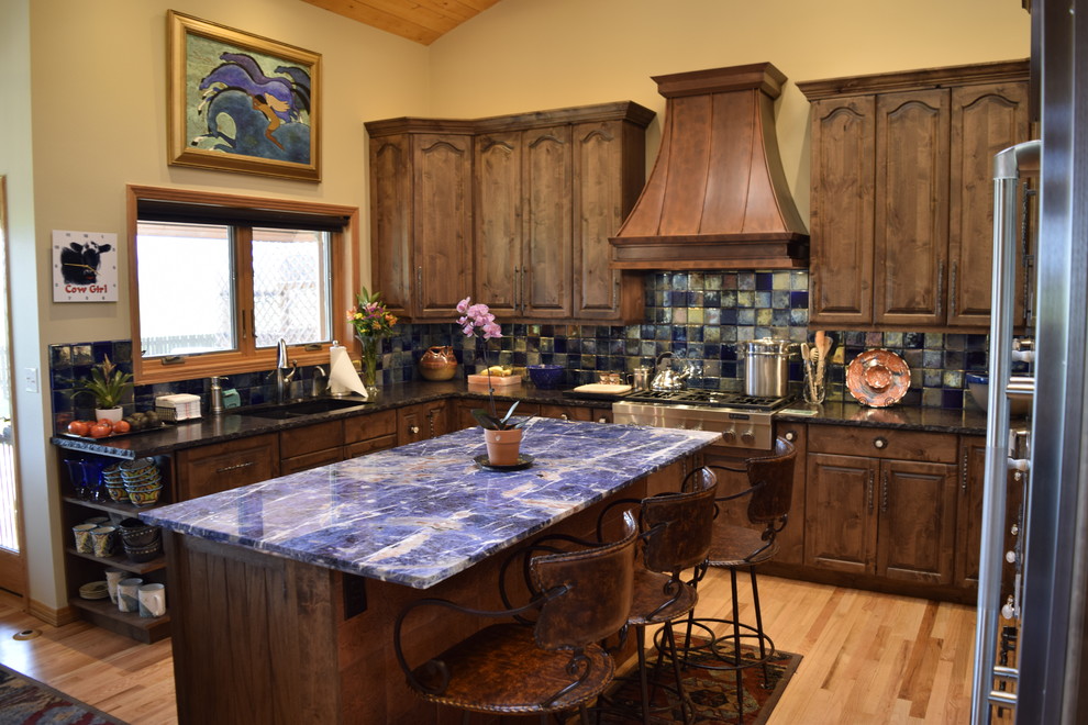 Photo of a mid-sized traditional u-shaped eat-in kitchen in Denver with an undermount sink, recessed-panel cabinets, dark wood cabinets, granite benchtops, multi-coloured splashback, glass tile splashback, stainless steel appliances, light hardwood floors and with island.