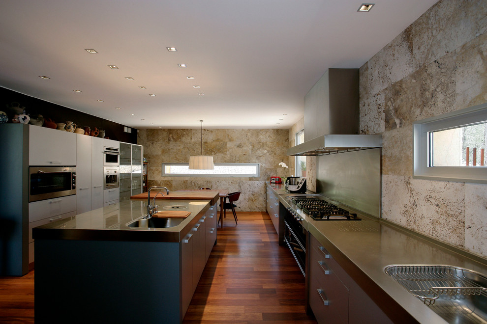 Photo of a large contemporary u-shaped eat-in kitchen in Barcelona with an integrated sink, flat-panel cabinets, grey cabinets, stainless steel benchtops, brown splashback, stone slab splashback, stainless steel appliances and with island.