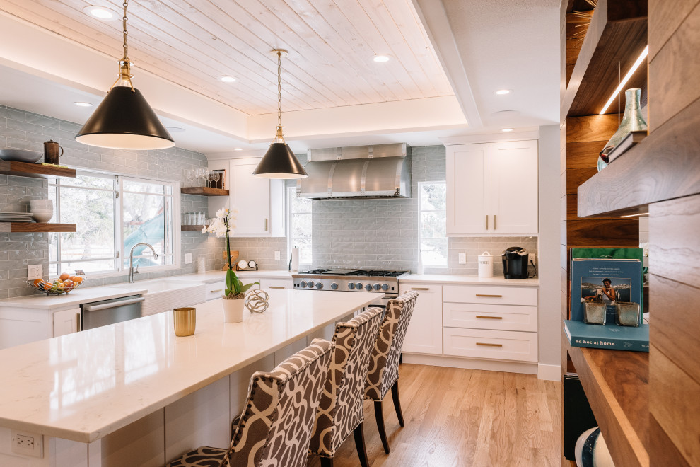 Mid-sized l-shaped eat-in kitchen in Denver with a farmhouse sink, shaker cabinets, white cabinets, quartz benchtops, grey splashback, glass tile splashback, stainless steel appliances, light hardwood floors, with island, beige floor, white benchtop and recessed.