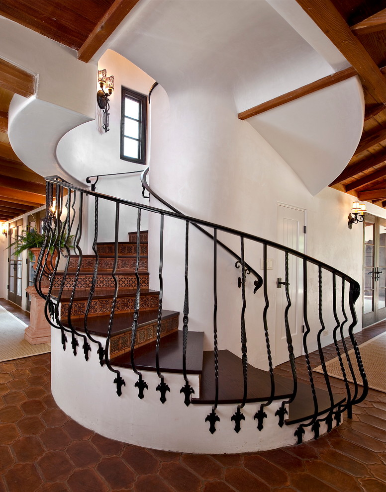 This is an example of a mediterranean wood curved staircase in Santa Barbara with terracotta risers and metal railing.
