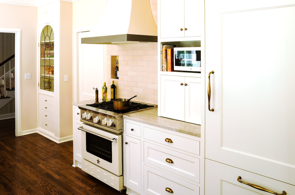 Photo of a mid-sized traditional u-shaped kitchen pantry in Portland with a double-bowl sink, shaker cabinets, white cabinets, solid surface benchtops, beige splashback, porcelain splashback, white appliances and dark hardwood floors.