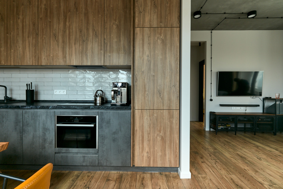 Photo of a mid-sized industrial single-wall open plan kitchen in Moscow with flat-panel cabinets, solid surface benchtops, white splashback, ceramic splashback, black appliances, medium hardwood floors, no island and black benchtop.