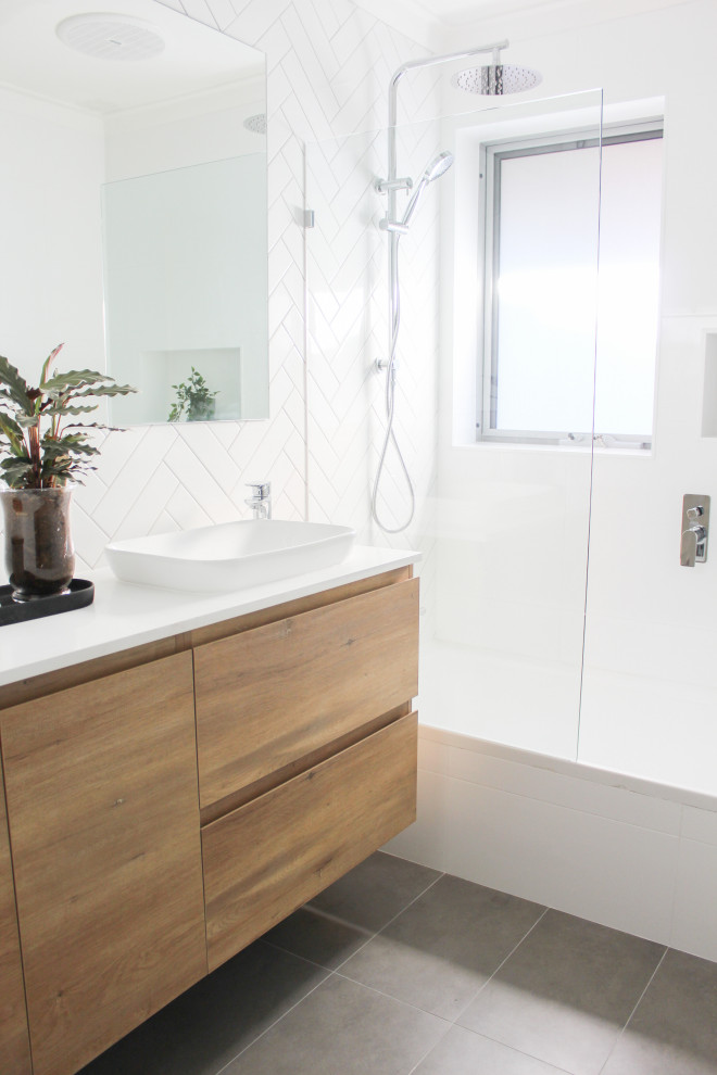 Photo of a small 3/4 bathroom in Perth with flat-panel cabinets, light wood cabinets, a drop-in tub, a shower/bathtub combo, white tile, ceramic tile, white walls, porcelain floors, a vessel sink, engineered quartz benchtops, grey floor, a hinged shower door, white benchtops, a single vanity and a floating vanity.