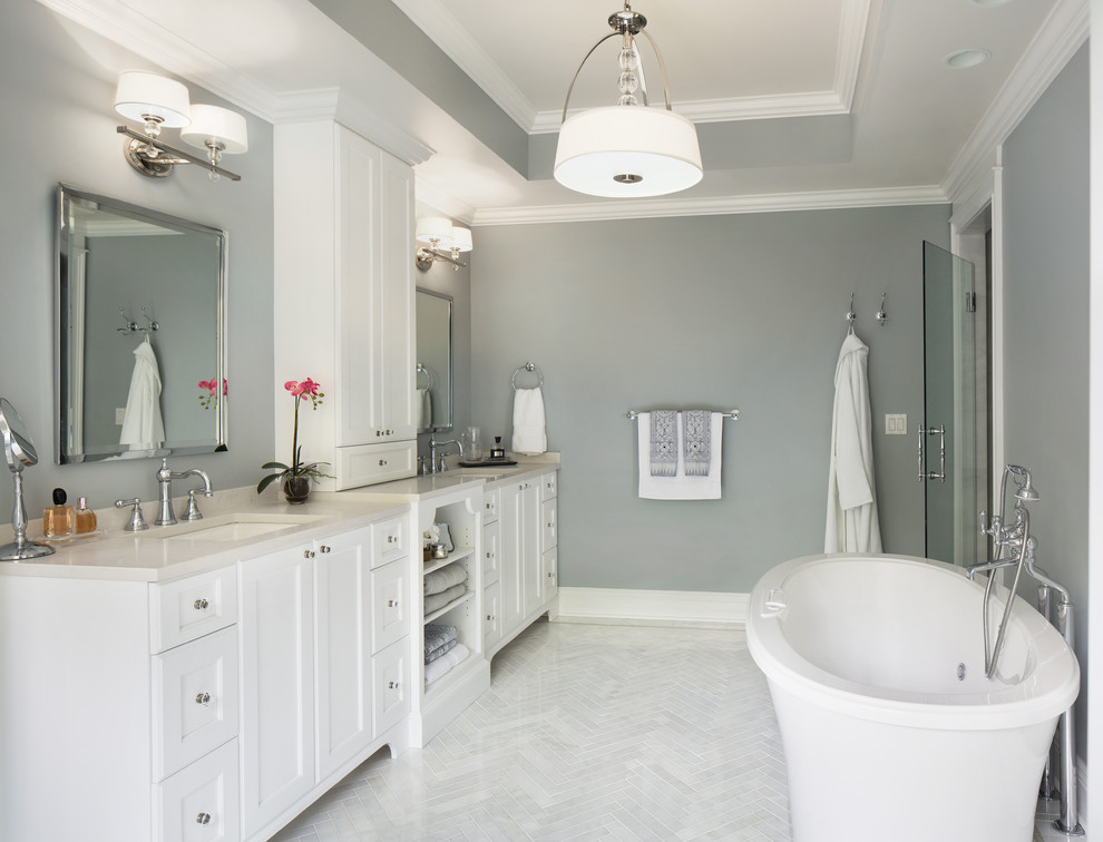 Inspiration for a large transitional master bathroom in New York with an undermount sink, recessed-panel cabinets, white cabinets, engineered quartz benchtops, a freestanding tub, an alcove shower, a one-piece toilet, white tile, stone tile, grey walls and marble floors.