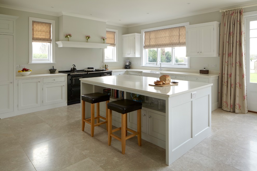 Design ideas for a mid-sized traditional l-shaped kitchen in Hampshire with a farmhouse sink, shaker cabinets, white cabinets, quartzite benchtops, black appliances, limestone floors, with island, beige floor and white benchtop.