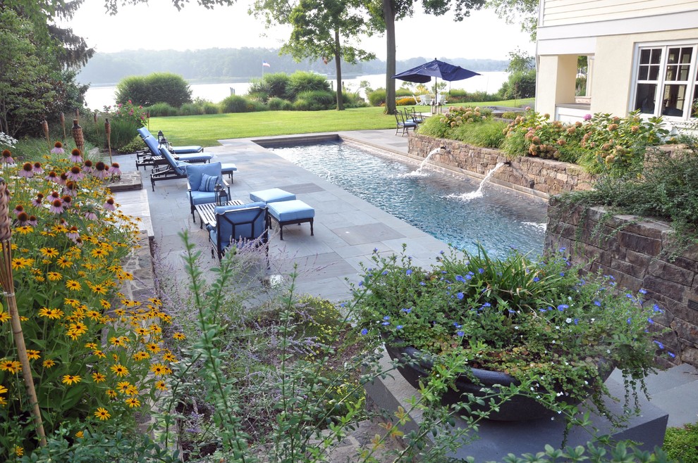 Photo of an expansive arts and crafts side yard rectangular lap pool in DC Metro with a water feature and natural stone pavers.
