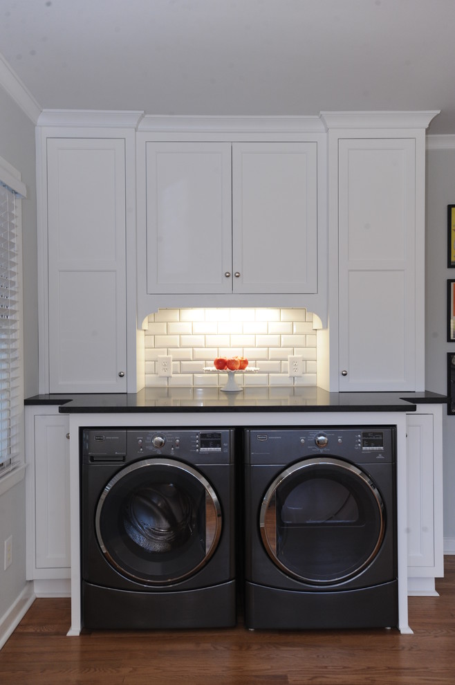 Inspiration for a large transitional single-wall utility room in Atlanta with an undermount sink, white cabinets, granite benchtops, white splashback, subway tile splashback, light hardwood floors, recessed-panel cabinets, grey walls, a side-by-side washer and dryer and brown floor.