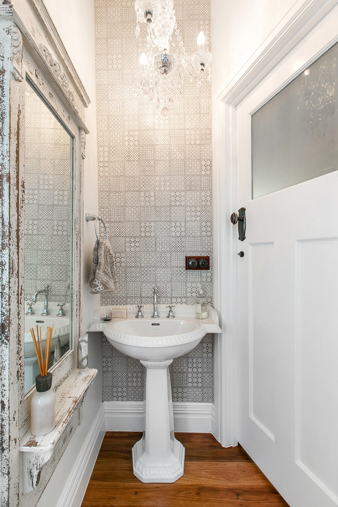Inspiration for a traditional powder room in Melbourne with a pedestal sink, a two-piece toilet, beige tile, porcelain tile, white walls and medium hardwood floors.