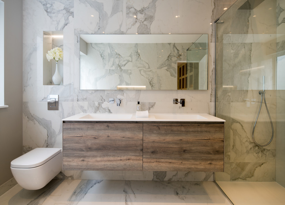 This is an example of a mid-sized contemporary master bathroom in London with dark wood cabinets, a freestanding tub, an open shower, a wall-mount toilet, gray tile, porcelain tile, grey walls, porcelain floors, an integrated sink, engineered quartz benchtops, grey floor, an open shower, white benchtops and flat-panel cabinets.