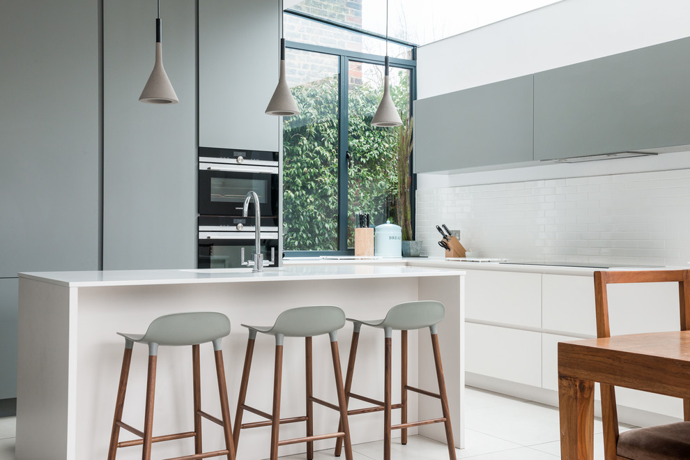 Large eclectic eat-in kitchen in London with a drop-in sink, flat-panel cabinets, grey cabinets, white splashback, ceramic splashback, stainless steel appliances, ceramic floors and a peninsula.
