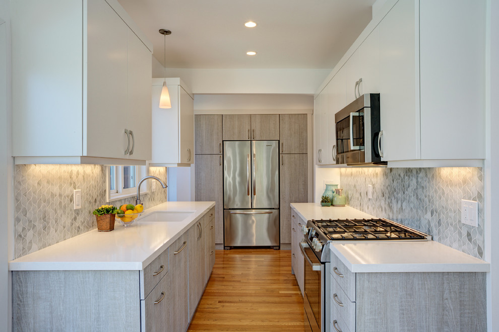 This is an example of a small contemporary u-shaped eat-in kitchen in San Francisco with a single-bowl sink, flat-panel cabinets, grey cabinets, solid surface benchtops, grey splashback, glass tile splashback, stainless steel appliances and light hardwood floors.