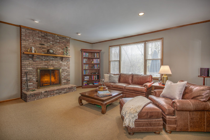 Photo of a mid-sized traditional enclosed family room in New York with beige walls, carpet, a standard fireplace and a brick fireplace surround.