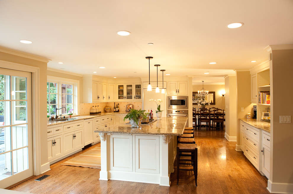Inspiration for a traditional l-shaped kitchen in Seattle with granite benchtops, recessed-panel cabinets, white cabinets, panelled appliances, an undermount sink, white splashback, ceramic splashback, with island and medium hardwood floors.