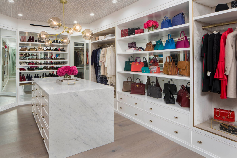This is an example of a large transitional women's dressing room in Los Angeles with shaker cabinets, white cabinets, light hardwood floors, beige floor and wallpaper.