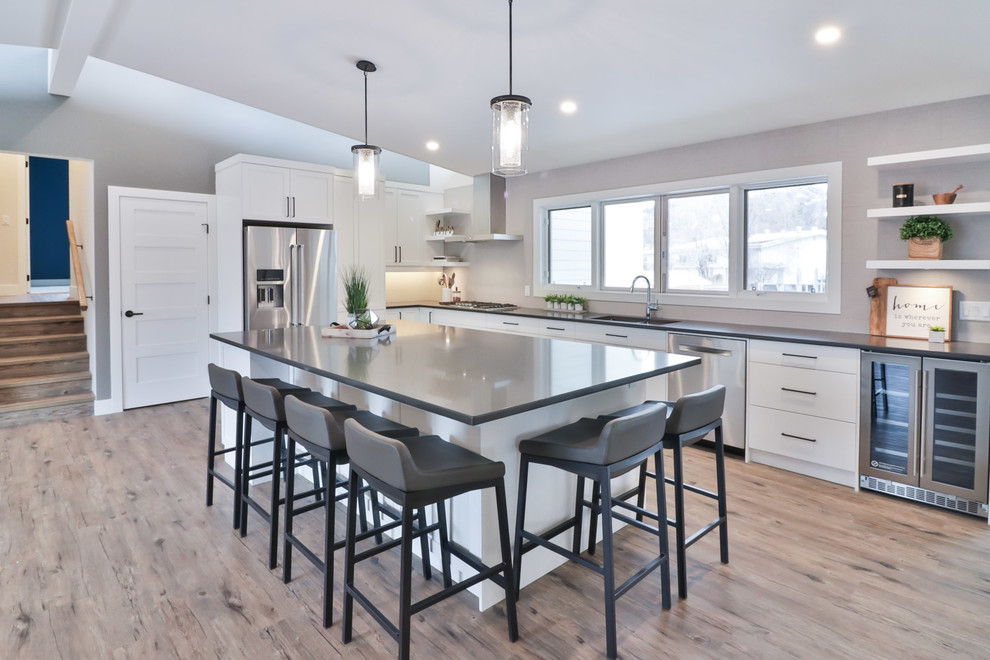 Inspiration for a large transitional l-shaped vinyl floor and brown floor open concept kitchen remodel with an undermount sink, flat-panel cabinets, white cabinets, quartz countertops, gray backsplash, porcelain backsplash, stainless steel appliances and an island