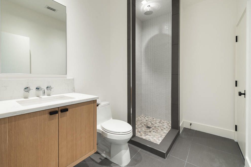 This is an example of a mid-sized modern kids bathroom in Dallas with flat-panel cabinets, brown cabinets, a corner shower, a one-piece toilet, white tile, ceramic tile, white walls, porcelain floors, an undermount sink, engineered quartz benchtops, grey floor, a hinged shower door and white benchtops.