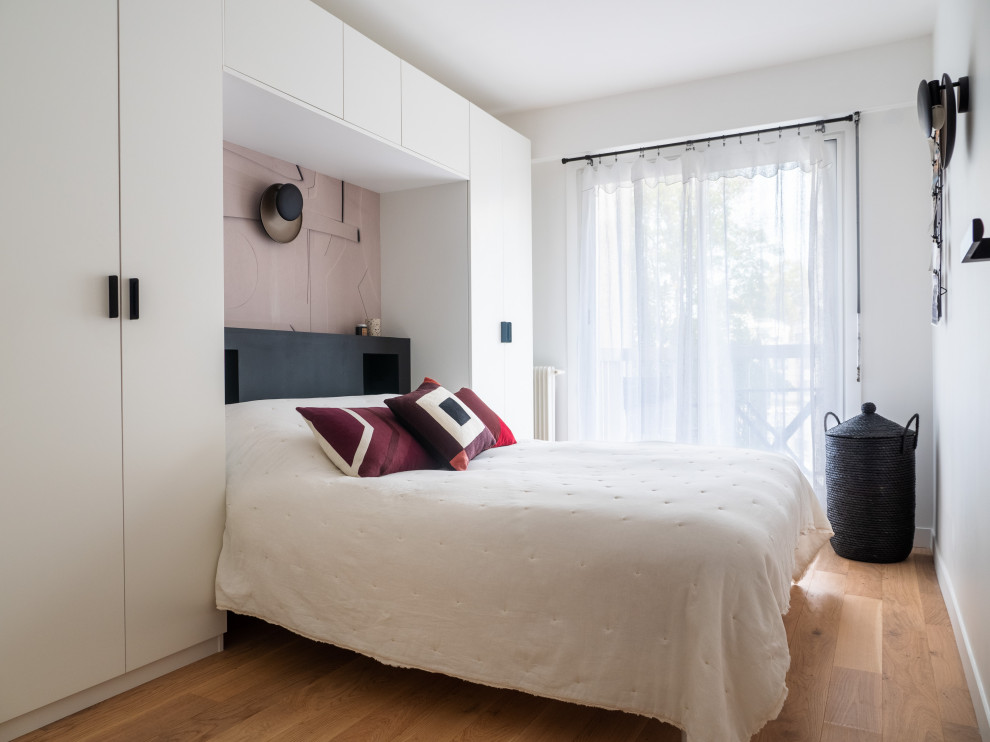 Modelo de dormitorio principal y blanco y madera minimalista de tamaño medio sin chimenea con paredes blancas, suelo de madera clara y suelo marrón