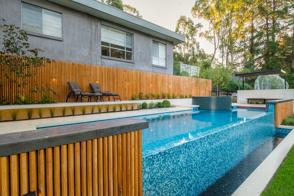 This is an example of a large contemporary backyard custom-shaped infinity pool in Melbourne with a hot tub and concrete slab.